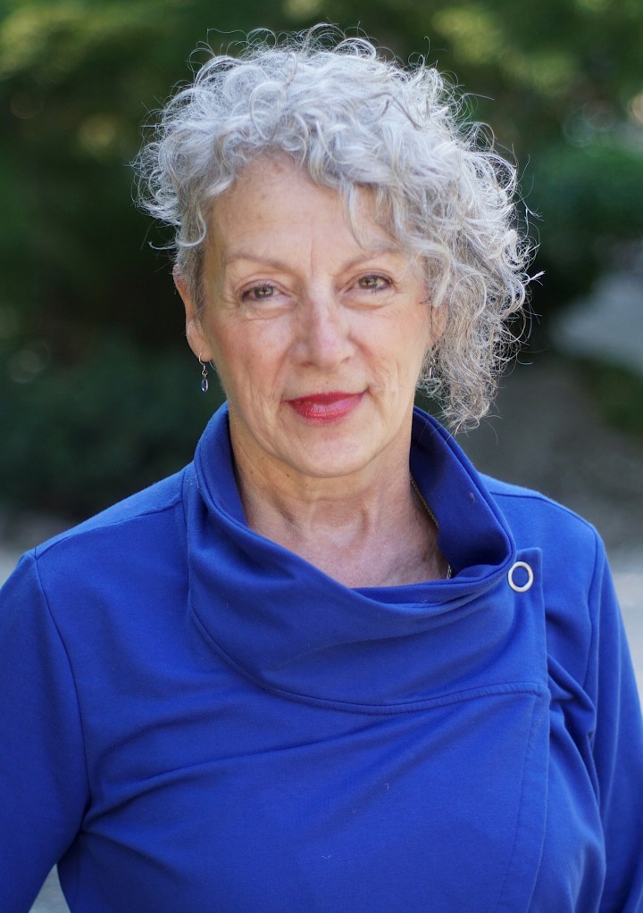 Headshot of Leslie Payne, an older white woman with short silver curly hair in a blue top.